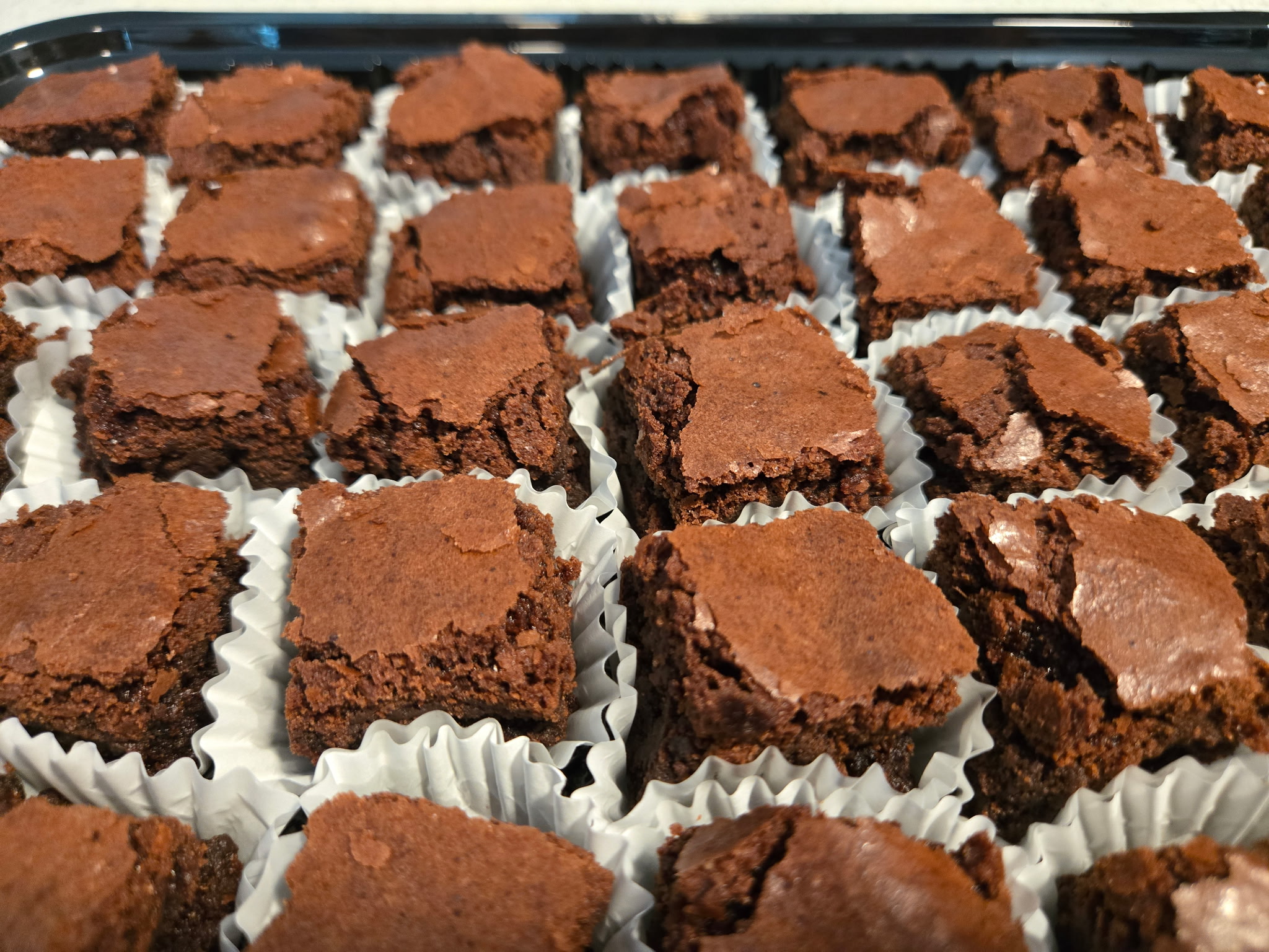 Tray of fudgy Koko's Kaleidoscope brownies with crackly tops in paper cups